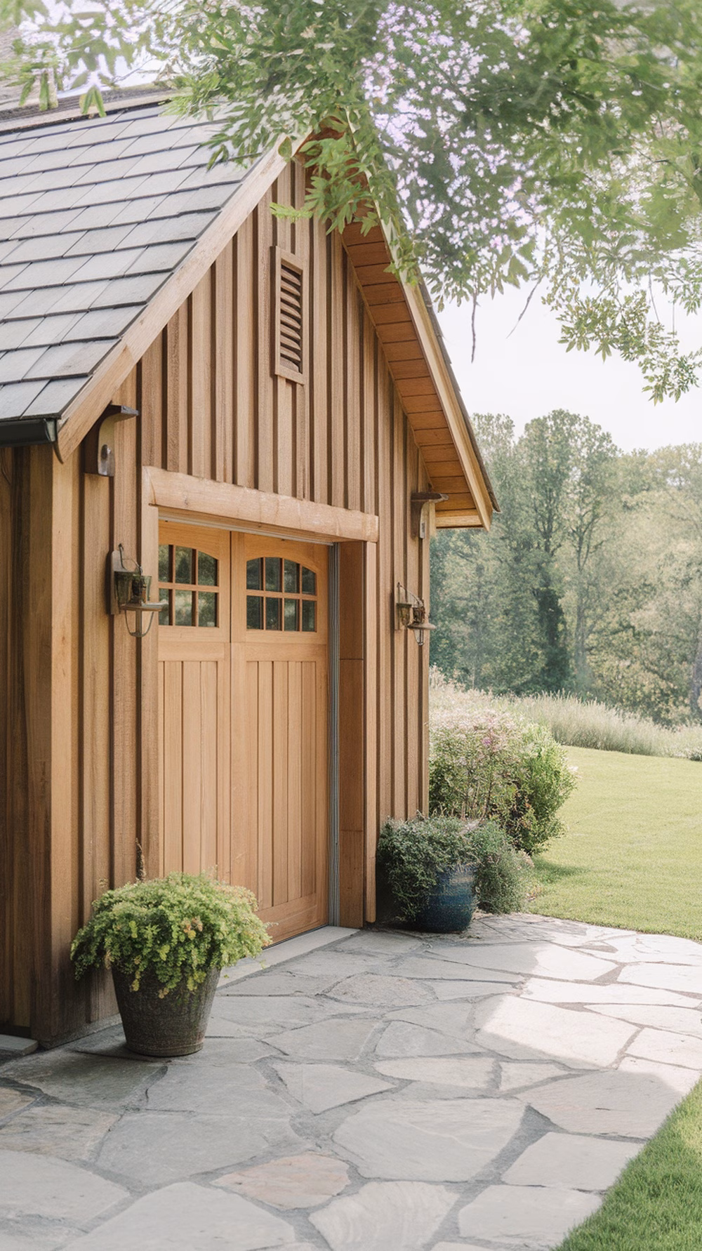 A rustic wooden garage with a sloped roof, large wooden door, and surrounding greenery.
