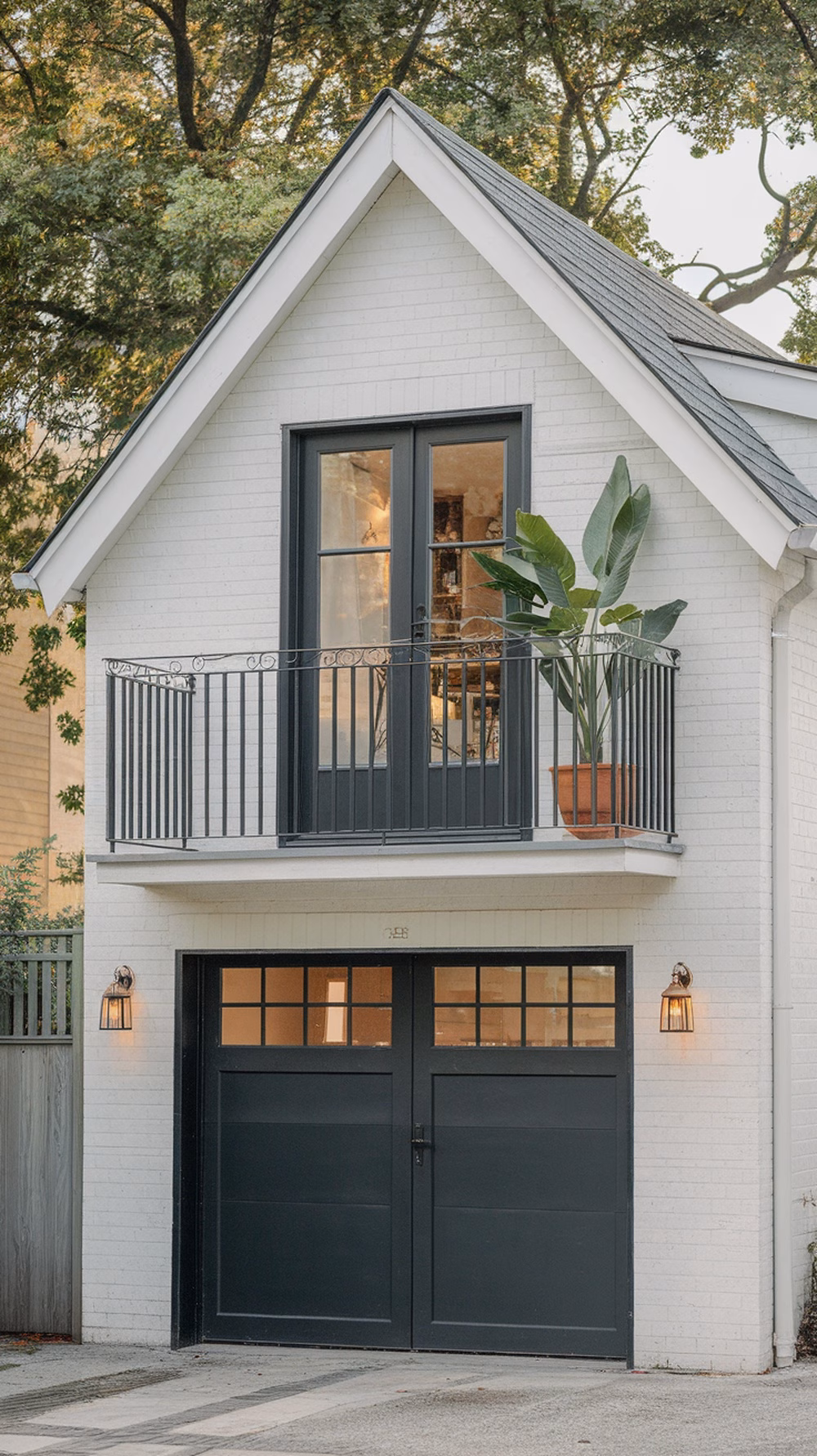 A stylish detached garage with a living space featuring a black door, large windows, and a balcony with a potted plant.